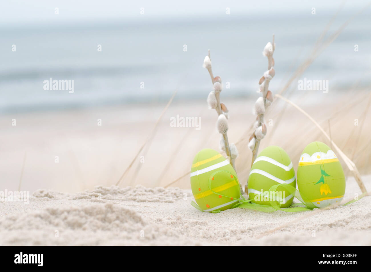 Easter decorated eggs and catkin on sand. Beach and ocean in the background Stock Photo