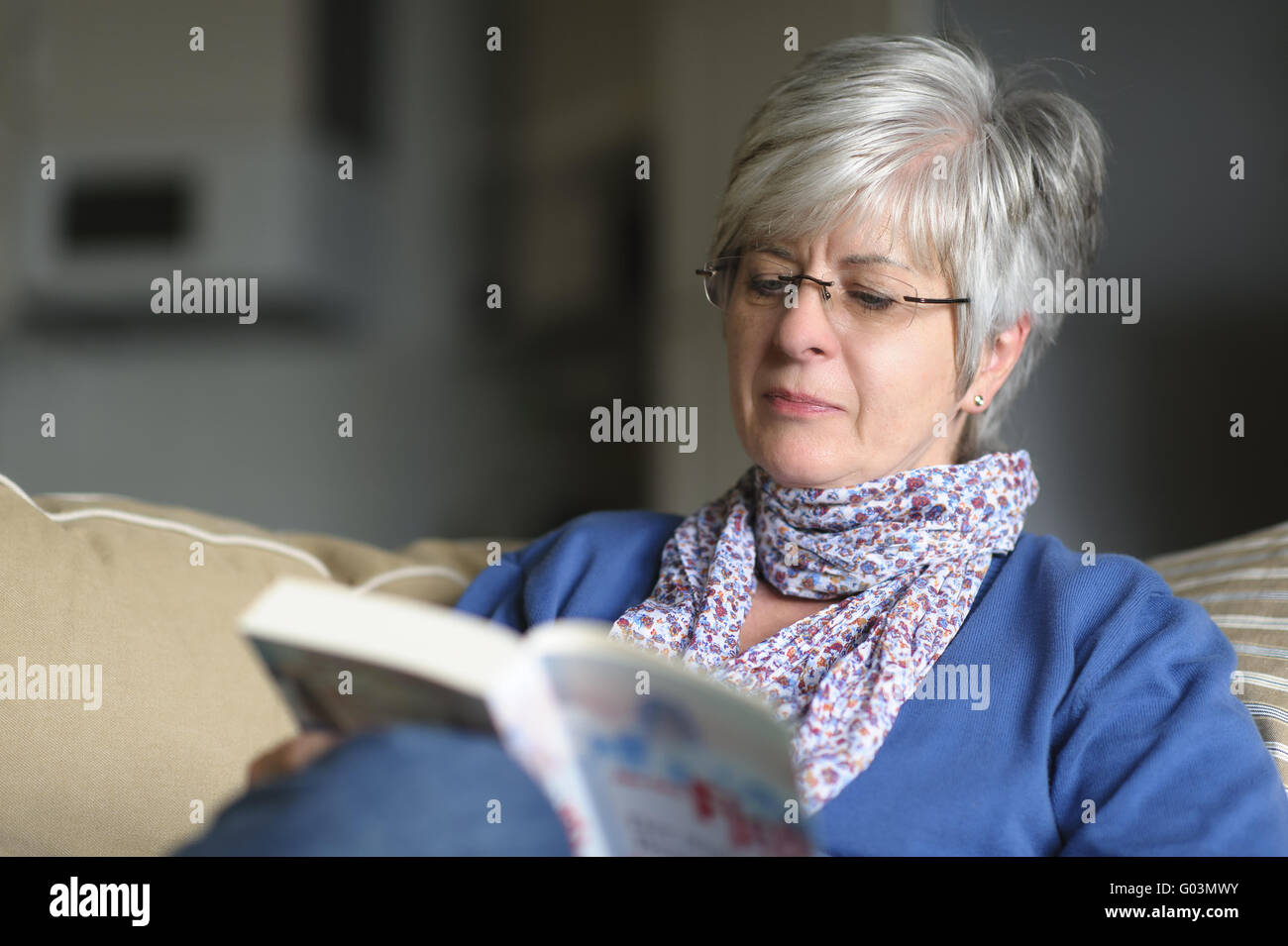 Woman sitting on a couch and reading a book Stock Photo