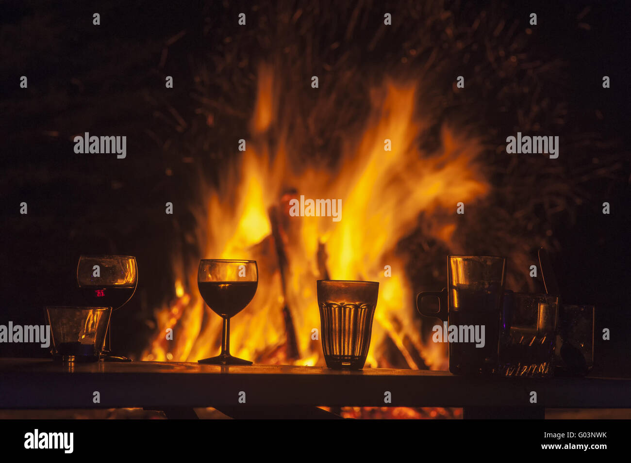 Table with glasses in front of a campfire at night Stock Photo