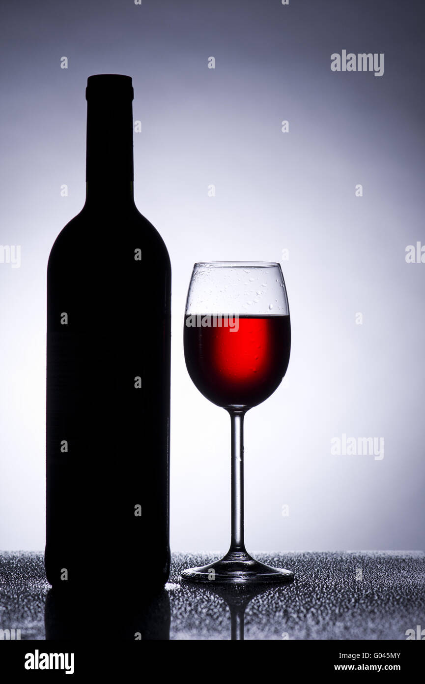 Red wine glass against the light with wine bottle Stock Photo