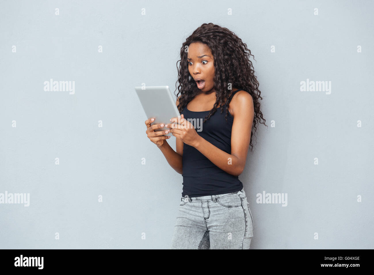 Shocked afro american woman using tablet computer over gray background Stock Photo