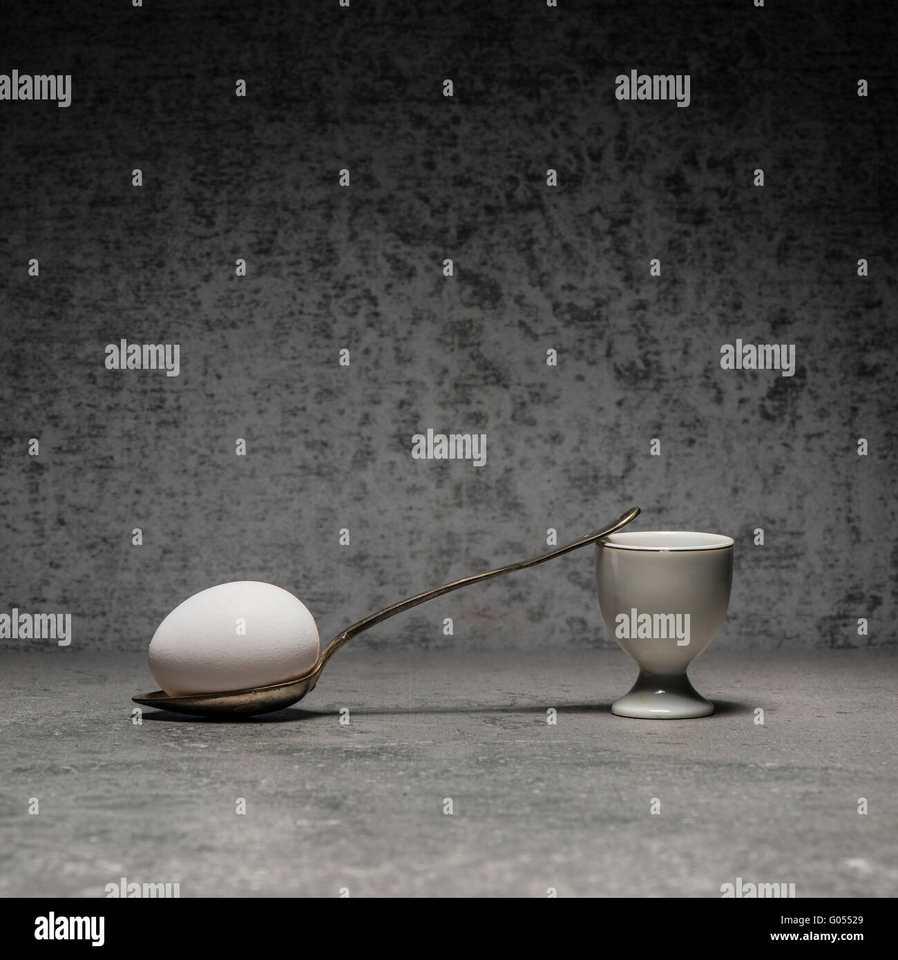 Egg, eggcup and spoon still life. Conceptual image with simplicity and copy space. Breakfast meal on stone table. Stock Photo