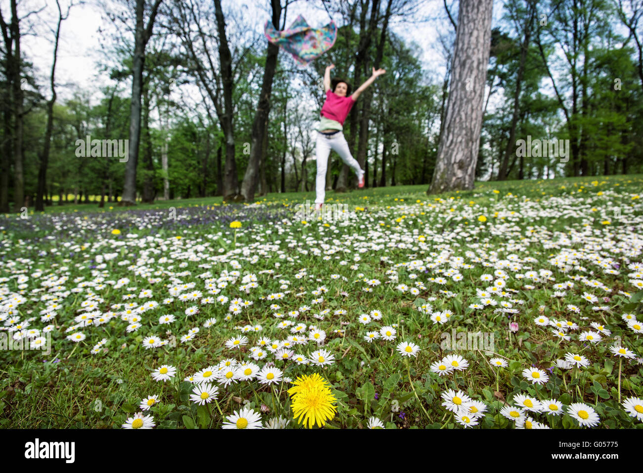 Young woman with silk scarf is jumping on the meadow full of ox-eye daisies and dandelions. Beauty, fashion and nature. Big fun. Stock Photo