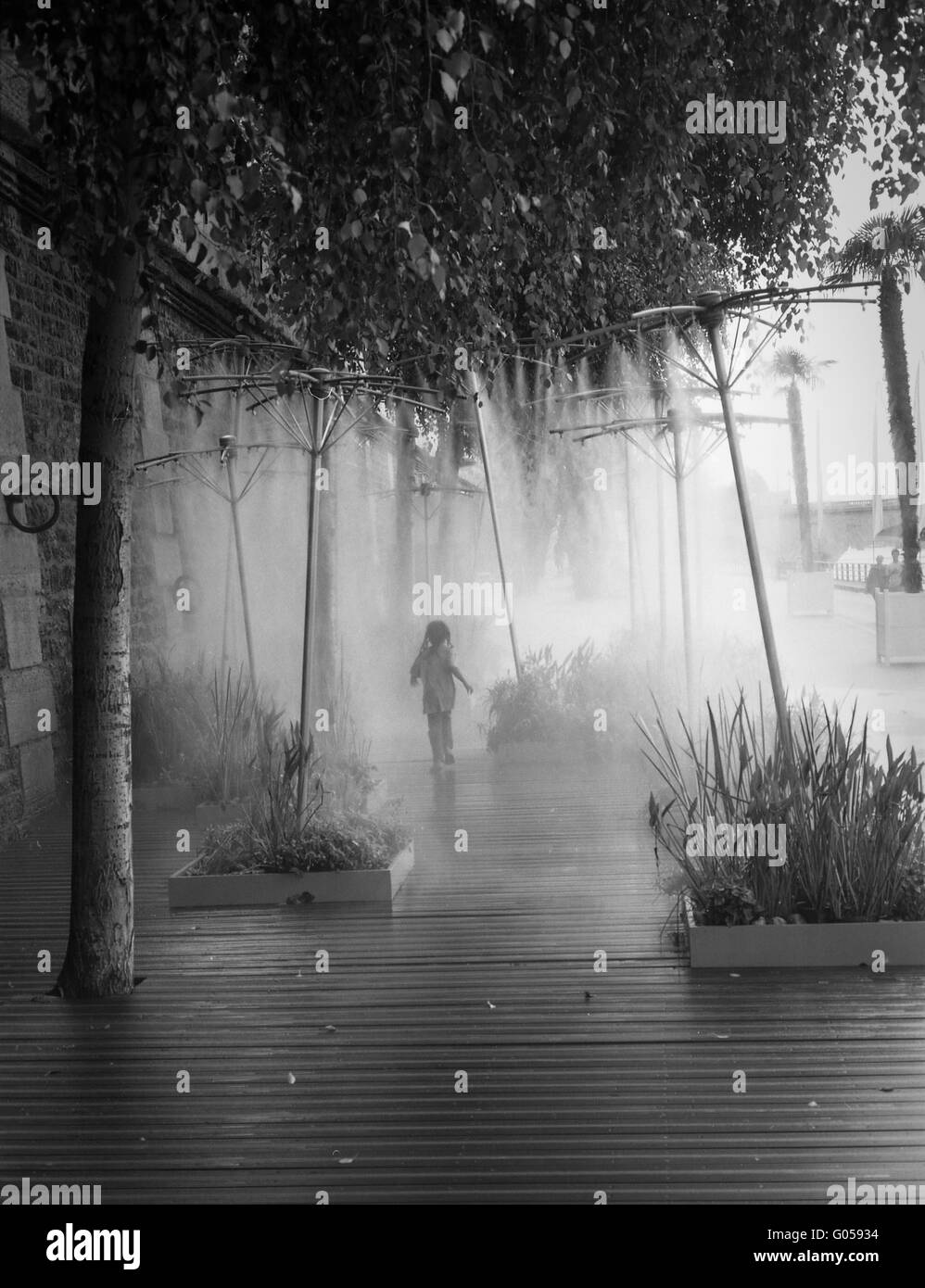 Young Girl Running Through Mist Sprinklers, River Stock Photo