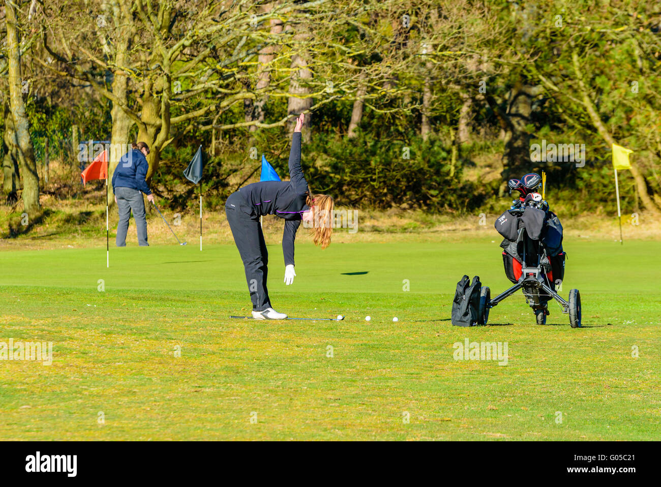 Falsterbo, Sweden - April 11, 2016: Young adult female golfer warming up before starting her round. Here seen doing stretch exer Stock Photo