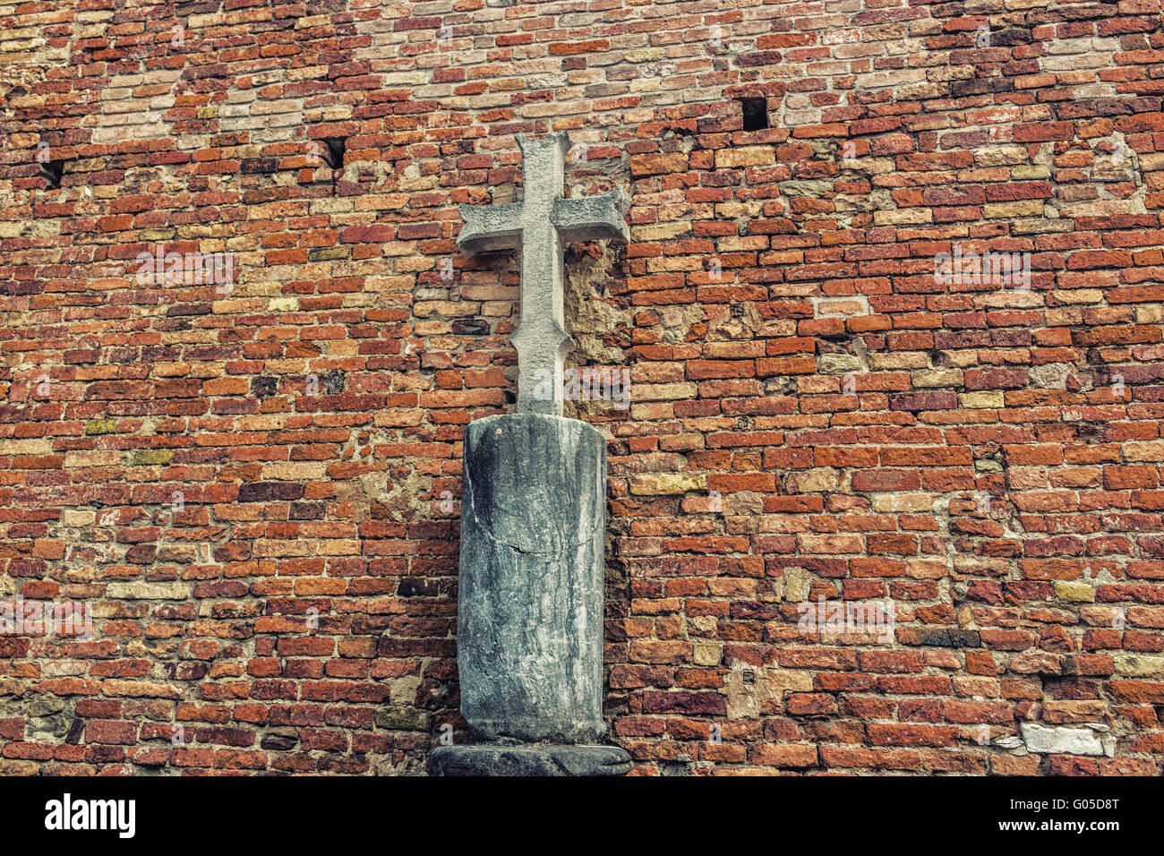 crucifix carved in stone with brick wall in the background Stock Photo
