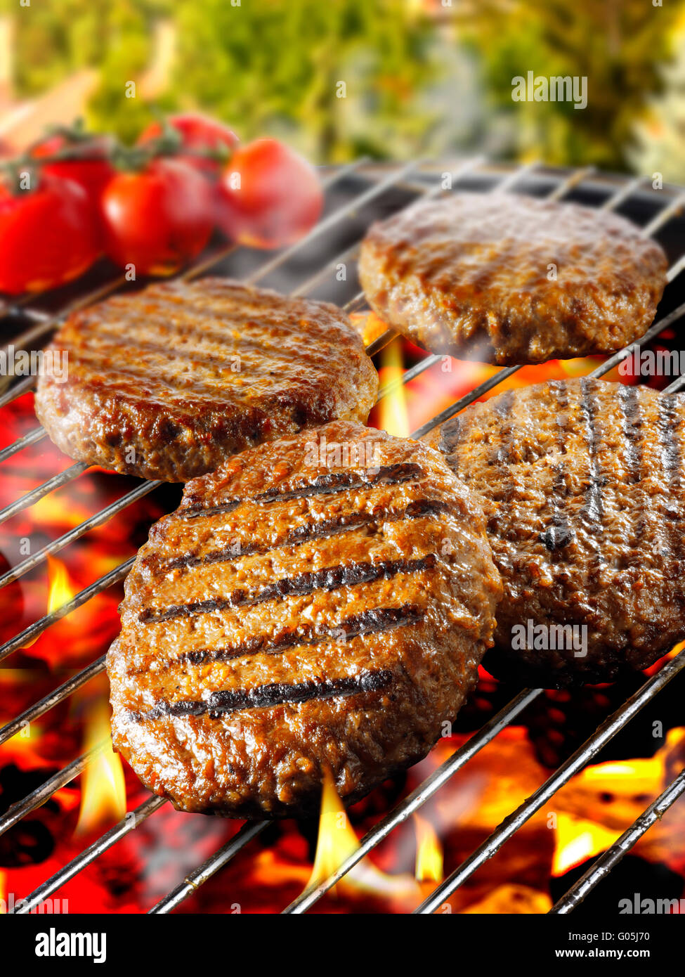 Beef burgers, hamburgers, being cooked on an open barbecue over hot flaming charcoals Stock Photo