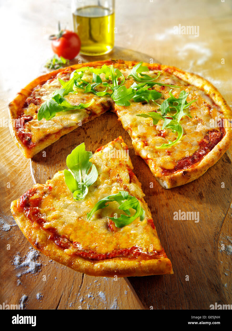 Cooked whole cheese and tomato Margherita pizza with rocket and a cut slice Stock Photo