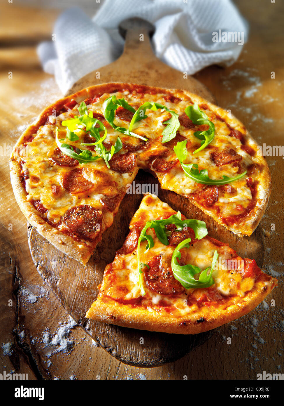 Cooked whole cheese and tomato pepperoni pizza with rocket and a cut slice Stock Photo