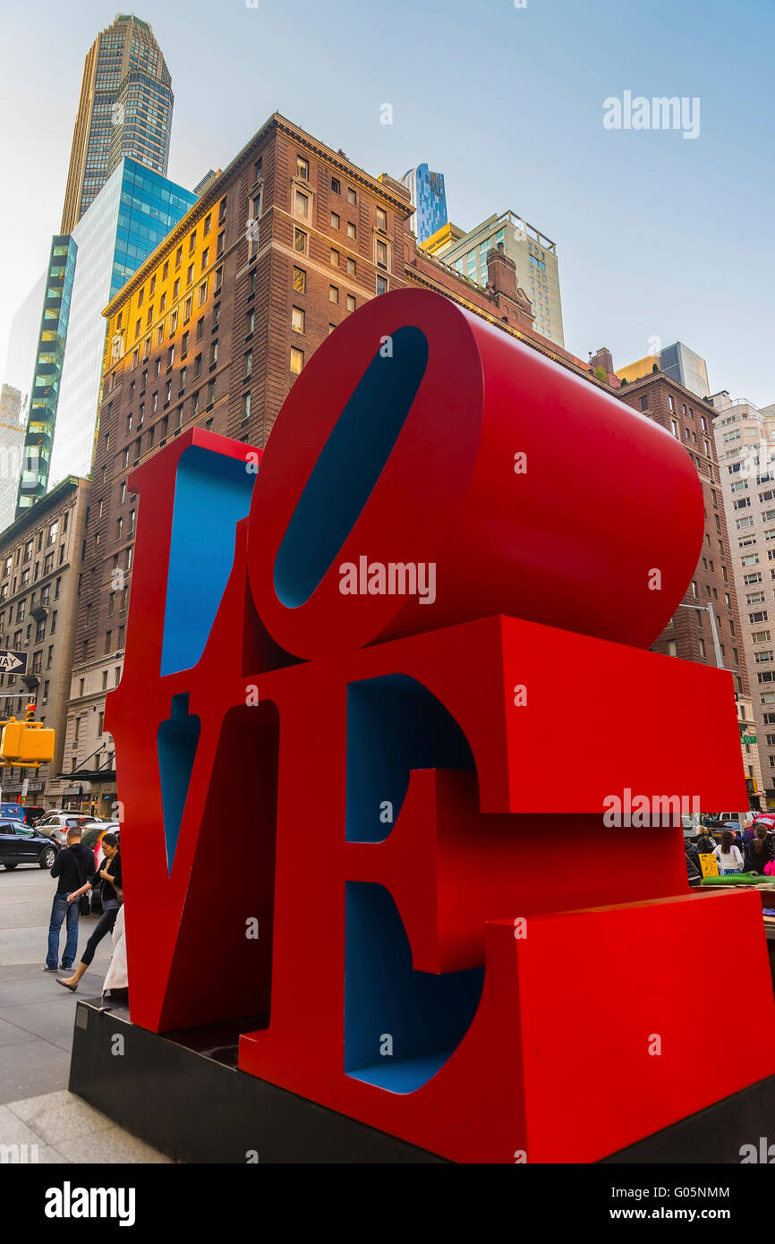 NEW YORK, USA - MAY 06, 2015: Love sculpture by American artist Robert Indiana and tourists passing by in Midtown Manhattan in New York, USA. The famous monument is located on 6th Avenue. Stock Photo