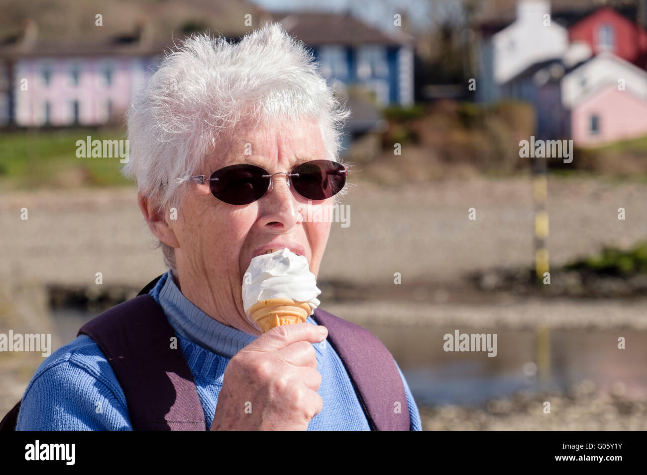 Authentic elderly senior woman older person retiree wearing dark sunglasses and eating an ice cream cone on a summers day. Aberaeron Wales UK Britain Stock Photo