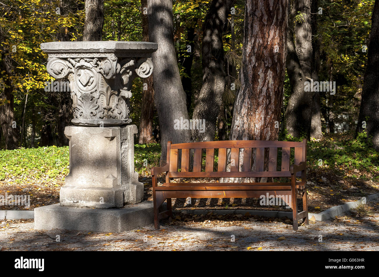 Wooden bench and stone capital in park Stock Photo