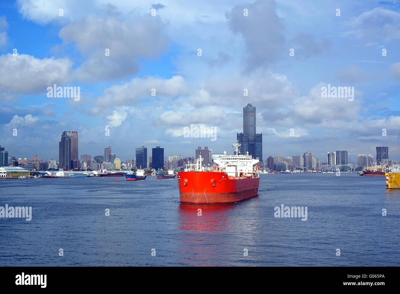 A large red oil tanker leaves Kaohsiung Port, in the background the skyline of the city. Stock Photo