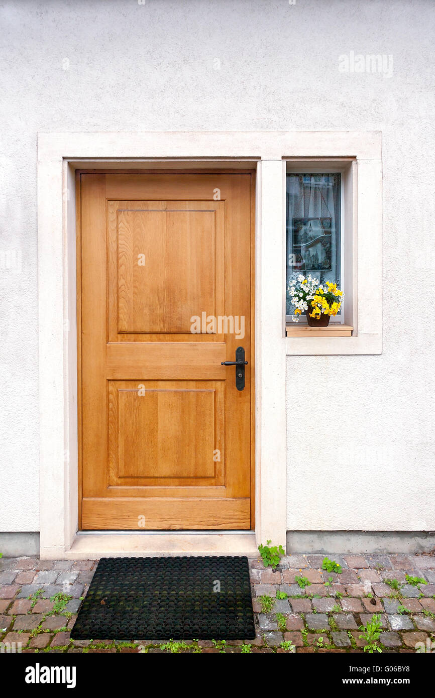 Brown simple wooden door with little window on the side yellow white flower on the window sill Stock Photo