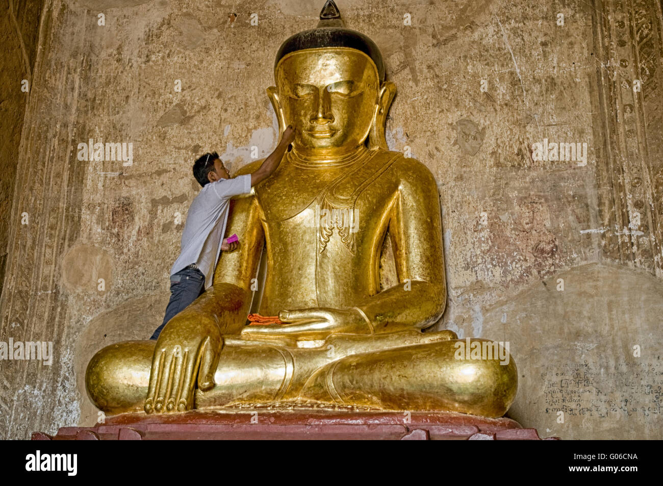 Man applies gold leaf to Buddha image, Burma Stock Photo