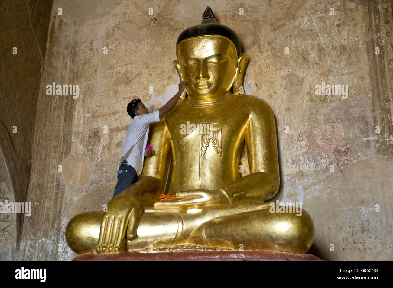 Man applies gold leaf to Buddha image, Burma Stock Photo