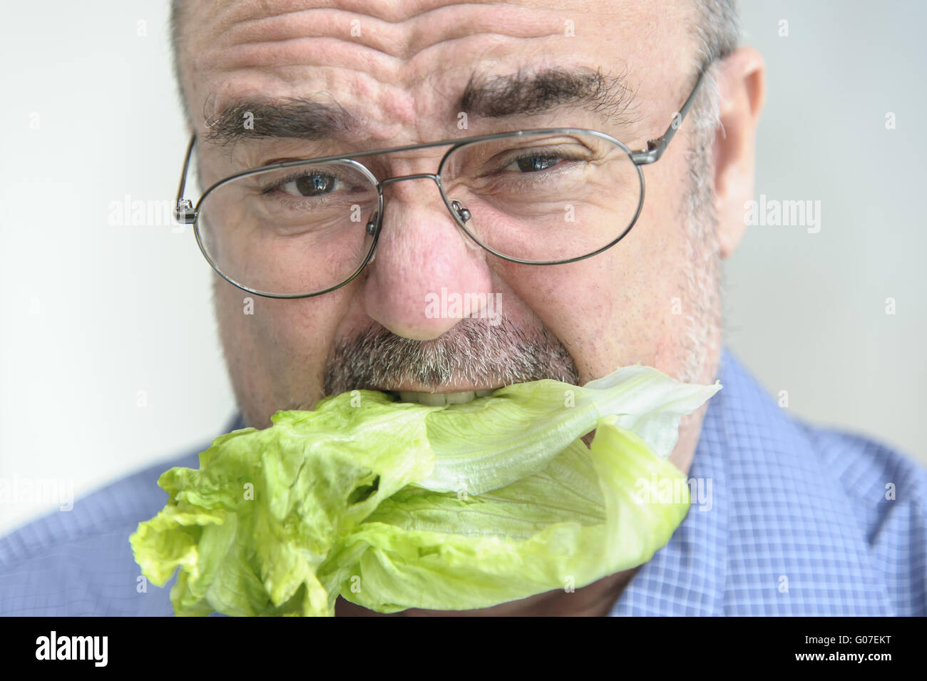 a senior chews with disgust on a lettuce leaf Stock Photo