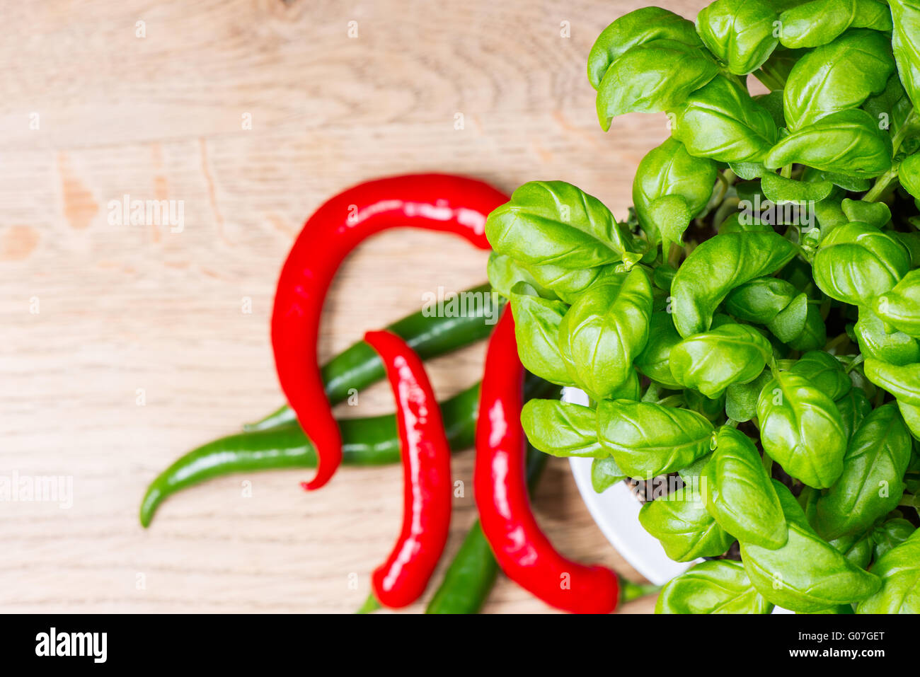 potted basil herb plant and chill peppers on wooden table Stock Photo