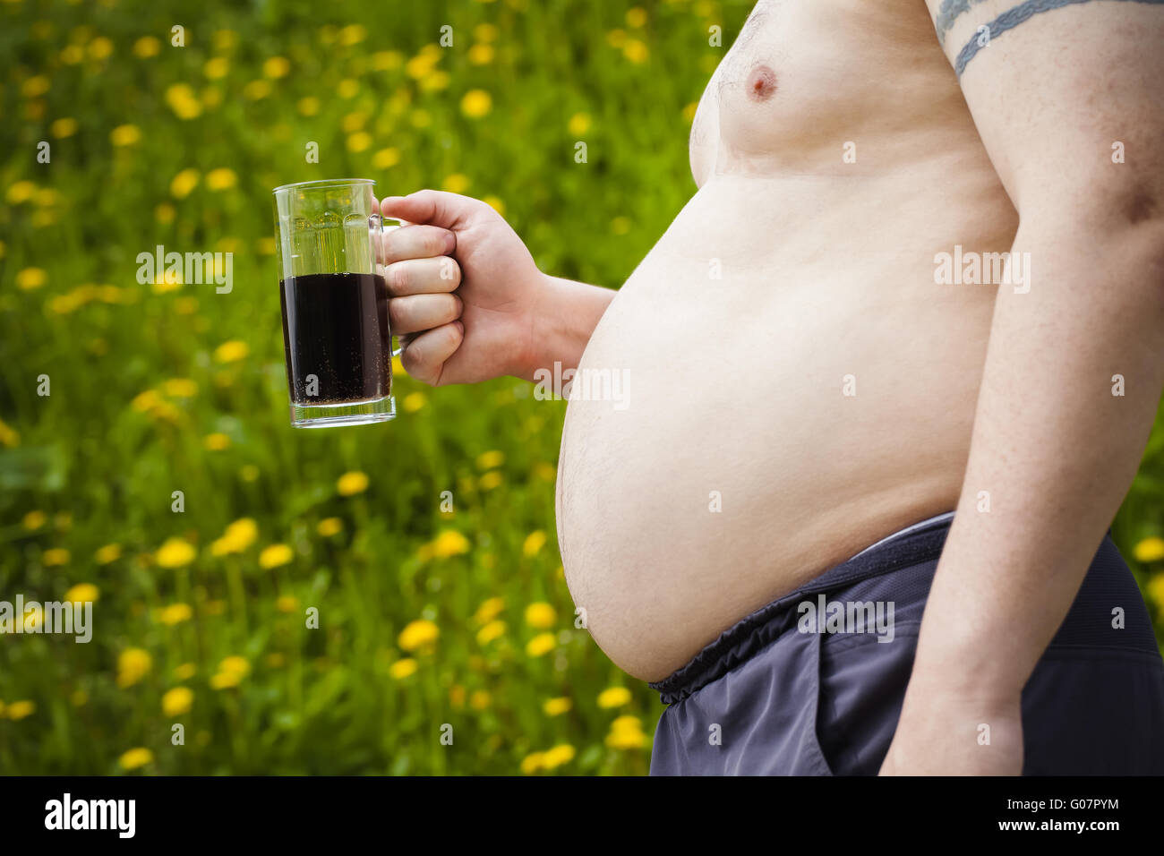 Fat man with a beer in hand on dandelion field ba Stock Photo