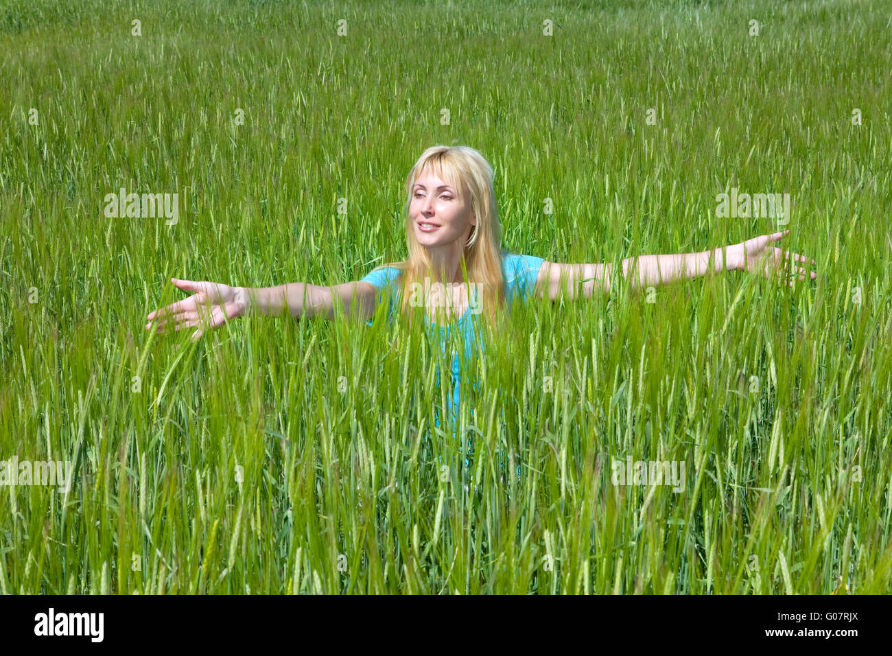 The happy young woman in the field of green ears Stock Photo