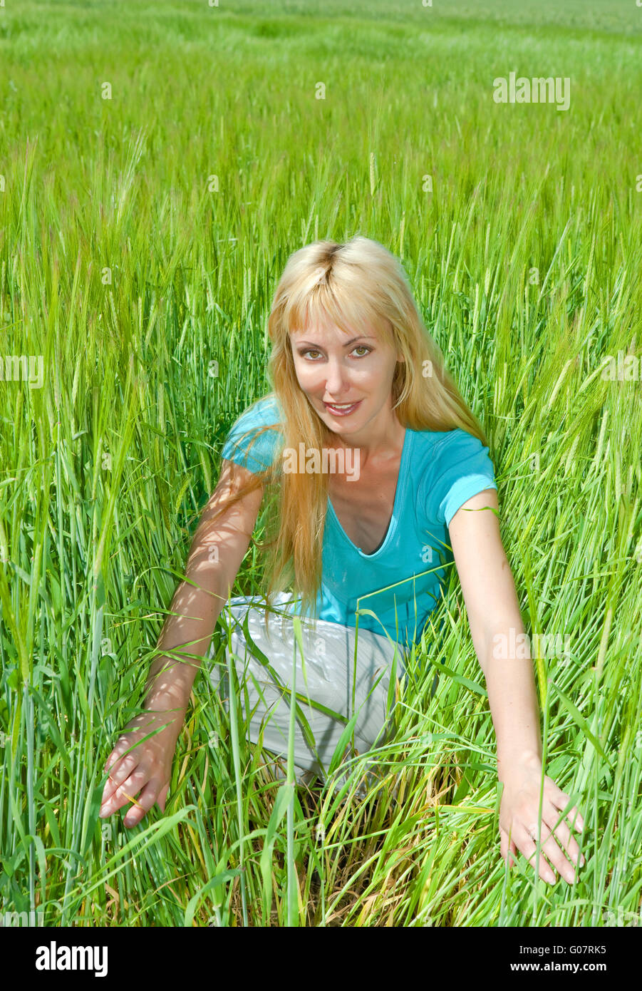 The happy young woman in the field of green ears Stock Photo