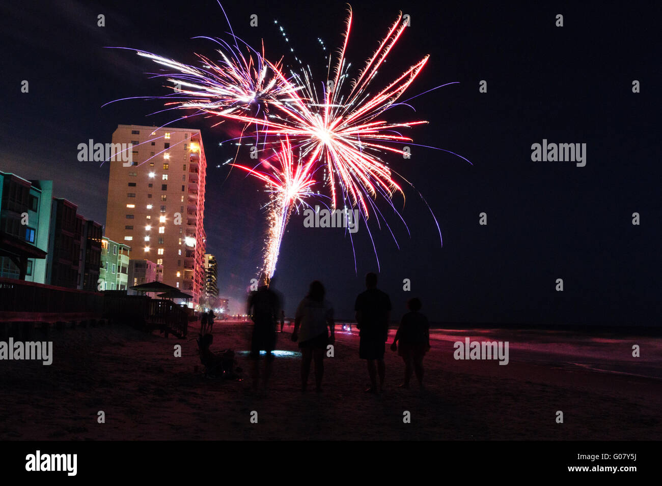 People stop to watch as a colorful amateur fireworks display breaks up the dark night sky on the beach in Garden City, SC. Stock Photo
