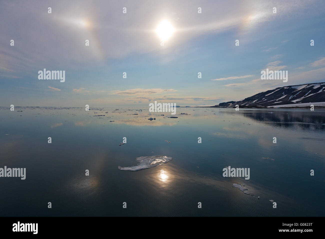 Parhelic circle and sun dogs in the sky and reflecting in the calm sea off Spitsbergen, Svalbard Stock Photo