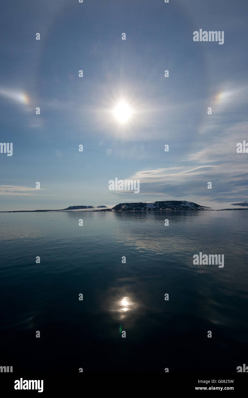 Parhelic circle and sun dogs in the sky and reflecting in the calm sea off Spitsbergen, Svalbard Stock Photo