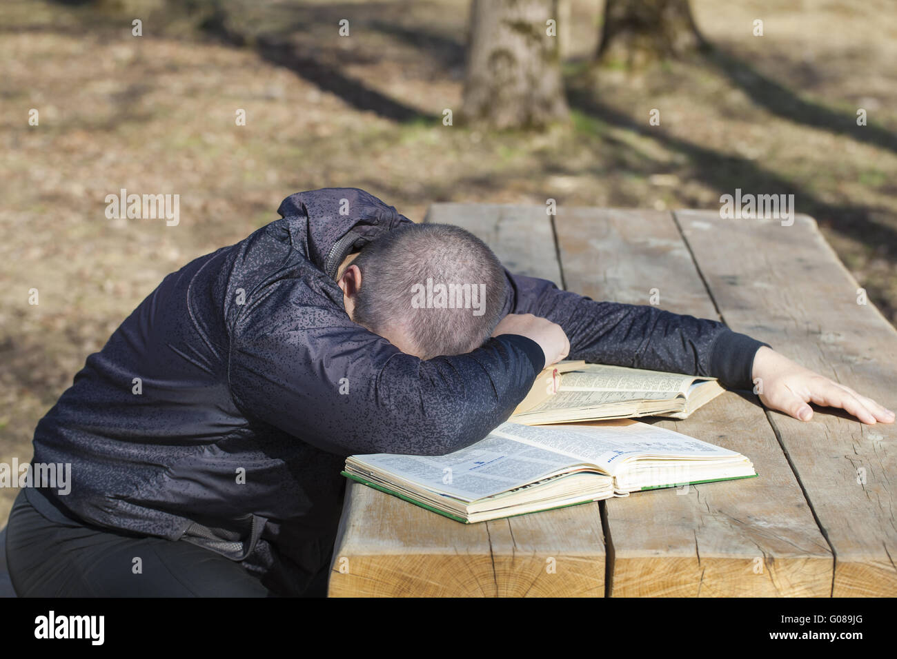Student lying asleep on books outside on a bench Stock Photo