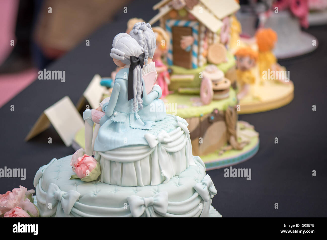 Cake decoration french wig couple man woman at Cake International – The Sugarcraft, Cake Decorating and Baking Show in London Stock Photo