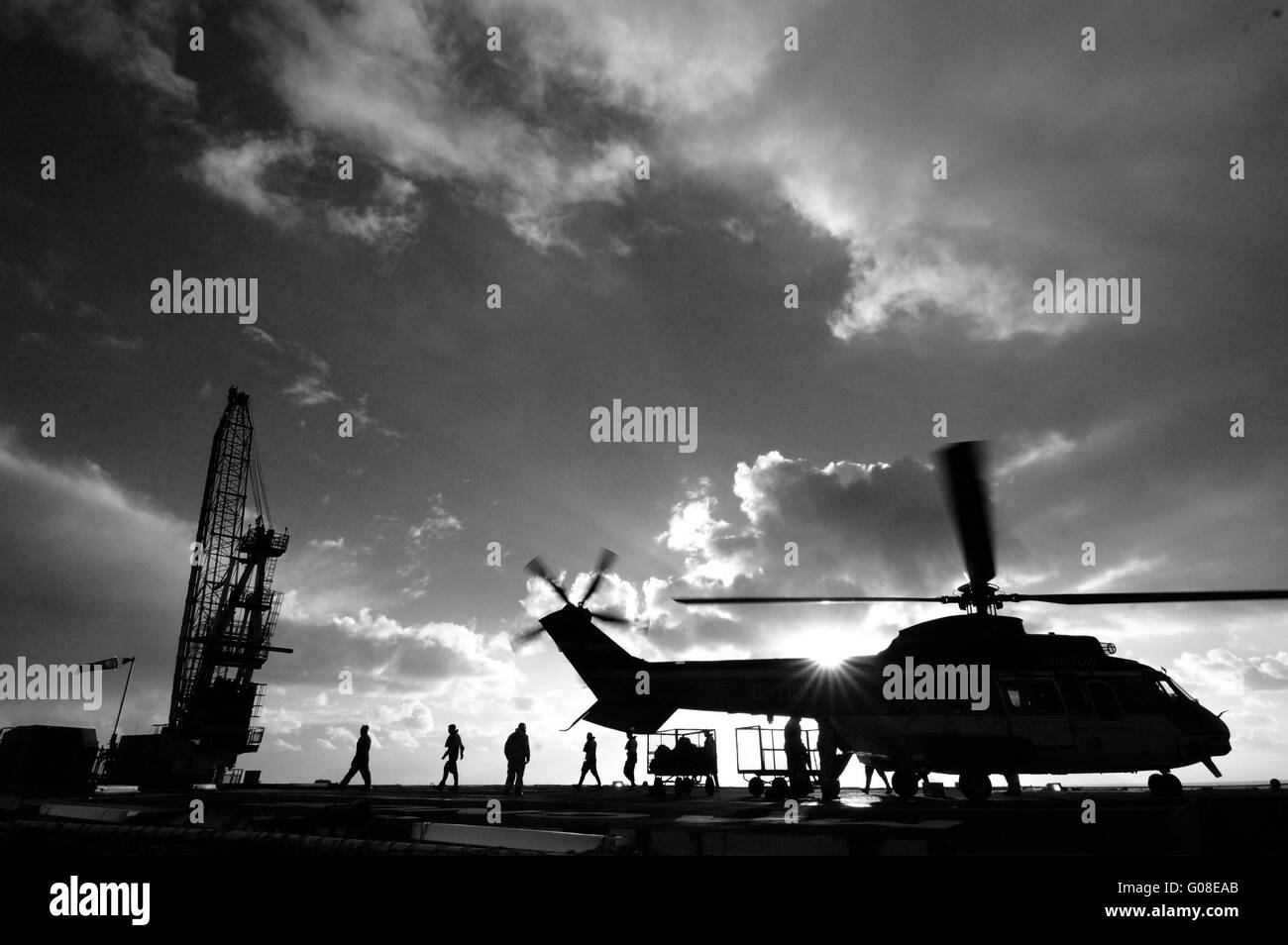 North sea chopper landing on helideck with the sun behind and crew on deck Stock Photo
