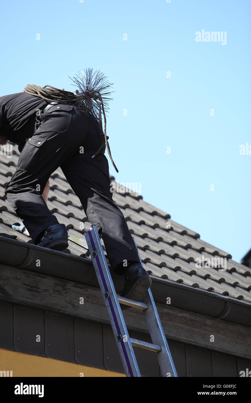 Chimney sweep climbing onto the roof of a house Stock Photo