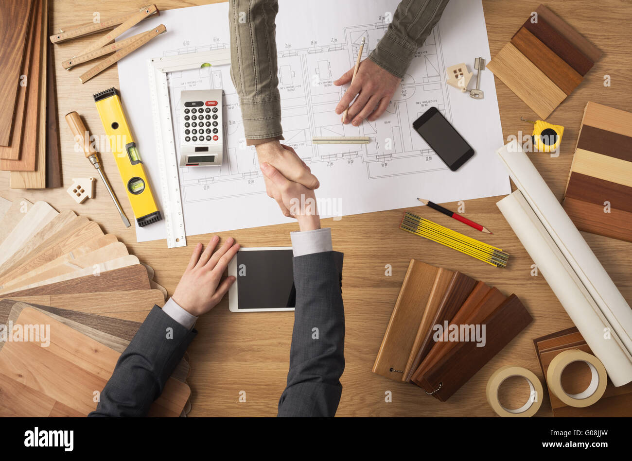 Architect and customer businessman shaking hands top view, desktop with building project, tools and wood swatches on background Stock Photo