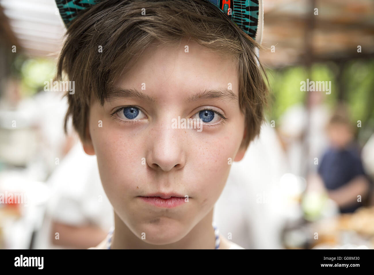 young boy with basecap looking into the camera, blurred people in background Stock Photo