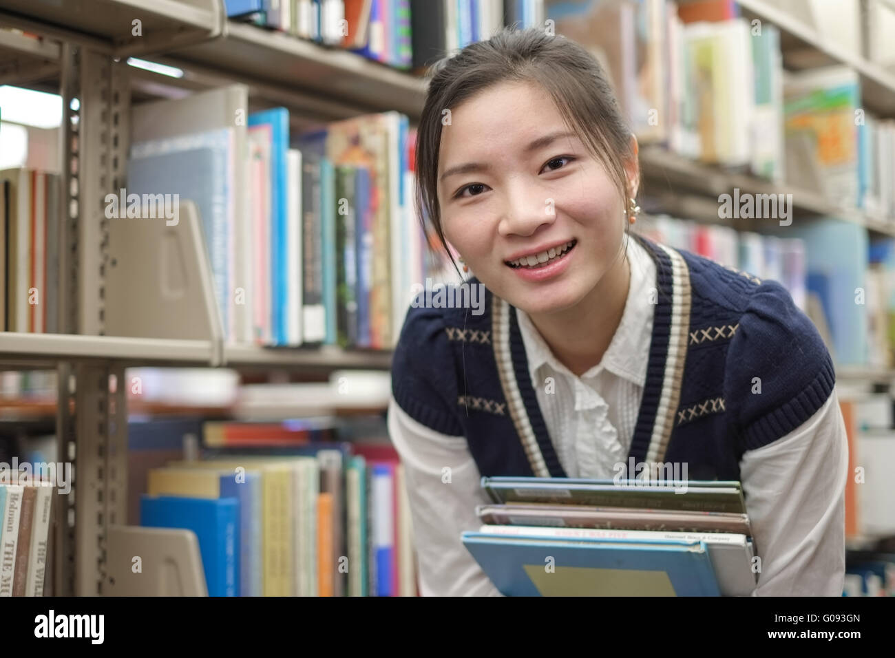 Young student holding books near bookshelf Stock Photo - Alamy
