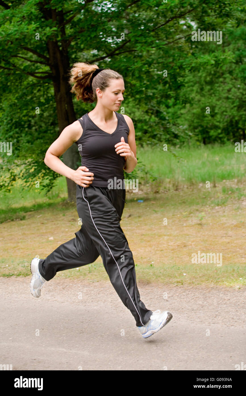 Sportive young woman running over a forrest road Stock Photo