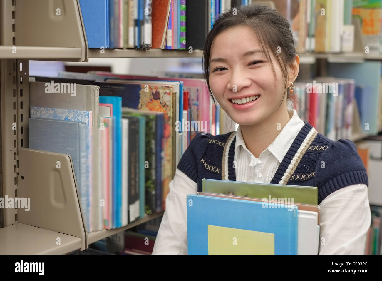 Young student holding books near bookshelf Stock Photo - Alamy