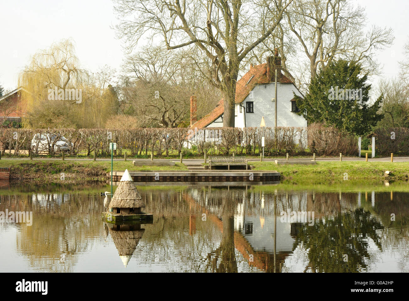 Berkshire - the village pond at Hurst - reflections - cottages - a thatched bird shelter floating - vantage point for a heron Stock Photo