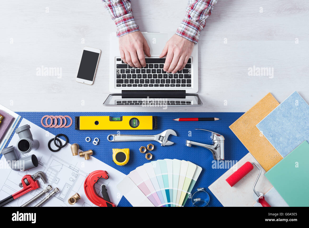 Male hands using a laptop next to plumbing work tools, tiles and swatches, online booking and home plumber service Stock Photo