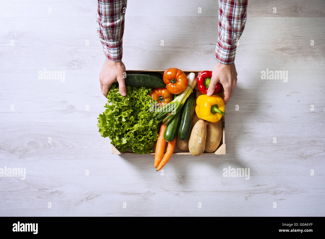Farmer holding a wooden crate filled with fresh harvested vegetables ...