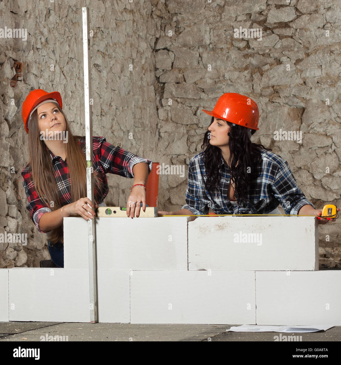 Two young long-haired woman built a new wall from blocks Stock Photo