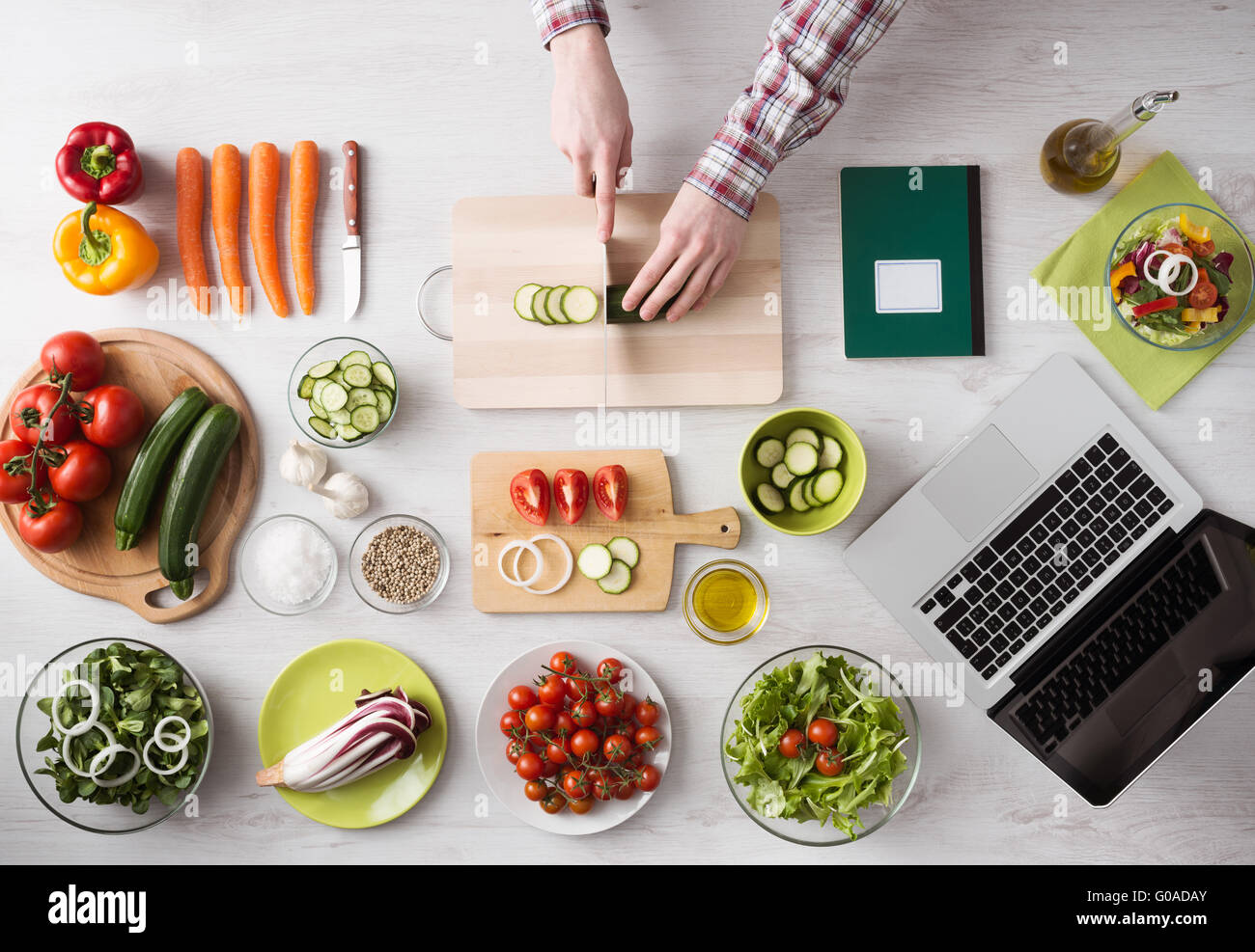 Man's hands cooking at home and chopping fresh vegetables on a cutting board, kitchen tools and food ingredients all around, top Stock Photo