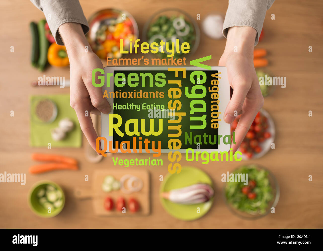Hands holding a digital touch screen tablet with fresh vegetables and kitchen utensils on background and healthy eating text Stock Photo
