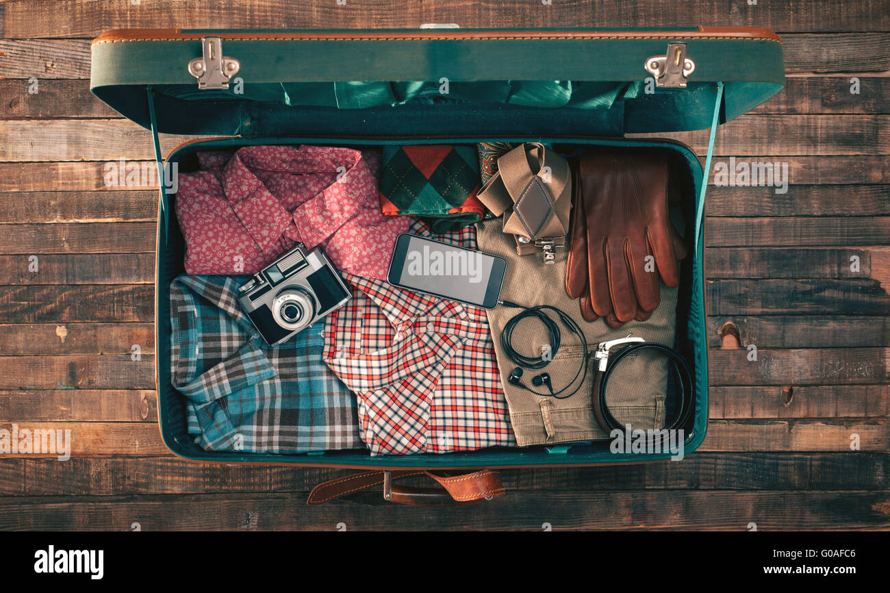 Vintage hipster traveler packing, open suitcase on a wooden table with clothing, camera and mobile phone, top view Stock Photo