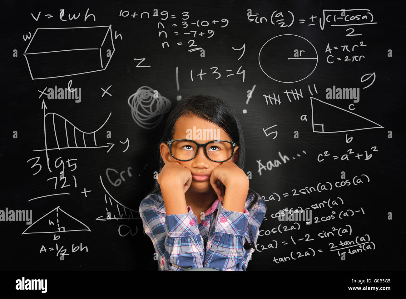 Little Asian student girl with glasses showing bored and tired over green chalkboard with math equivalents written on it Stock Photo