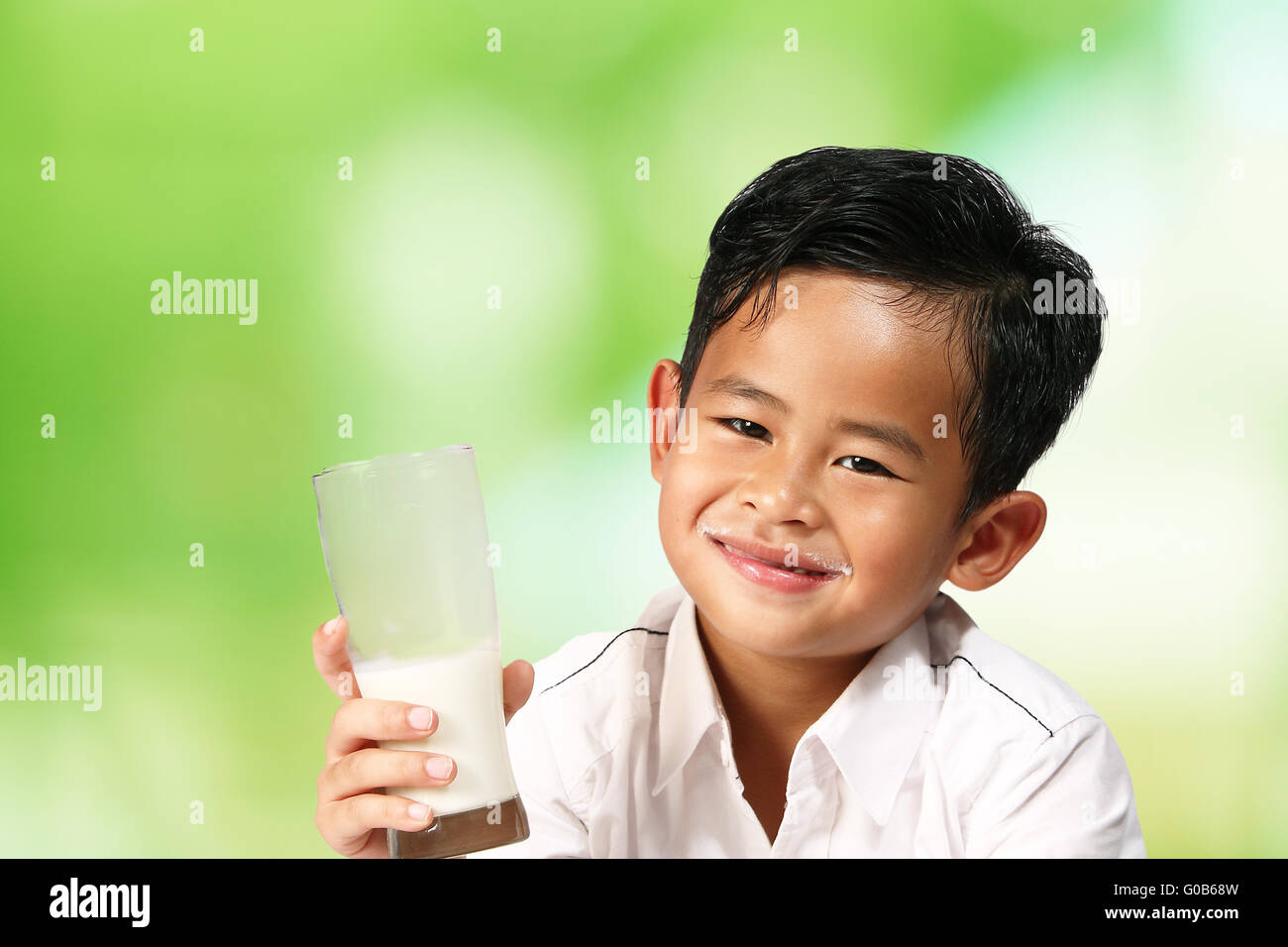 Young Asian boy smiling and holding a glass of milk over green blur background Stock Photo