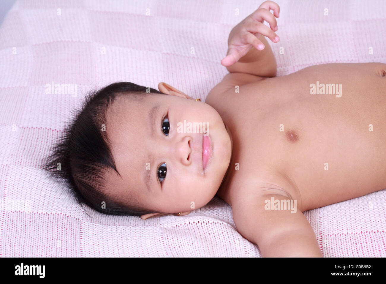 Portrait of cute little Asian baby girl lying down on bed and smiling to the camera Stock Photo