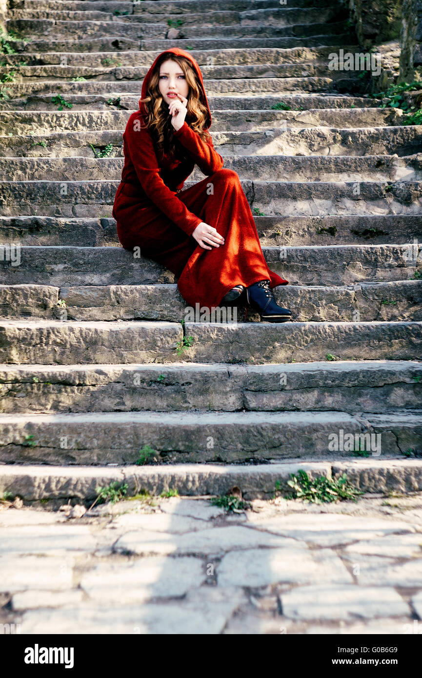 Beautiful woman in red dress sitting on old steps Stock Photo