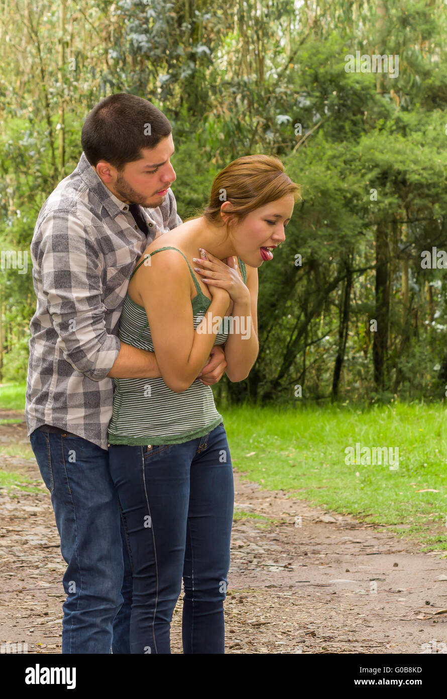 Young Woman Choking With Man Standing Behind Performing Heimlich Maneuver Park Environment And 
