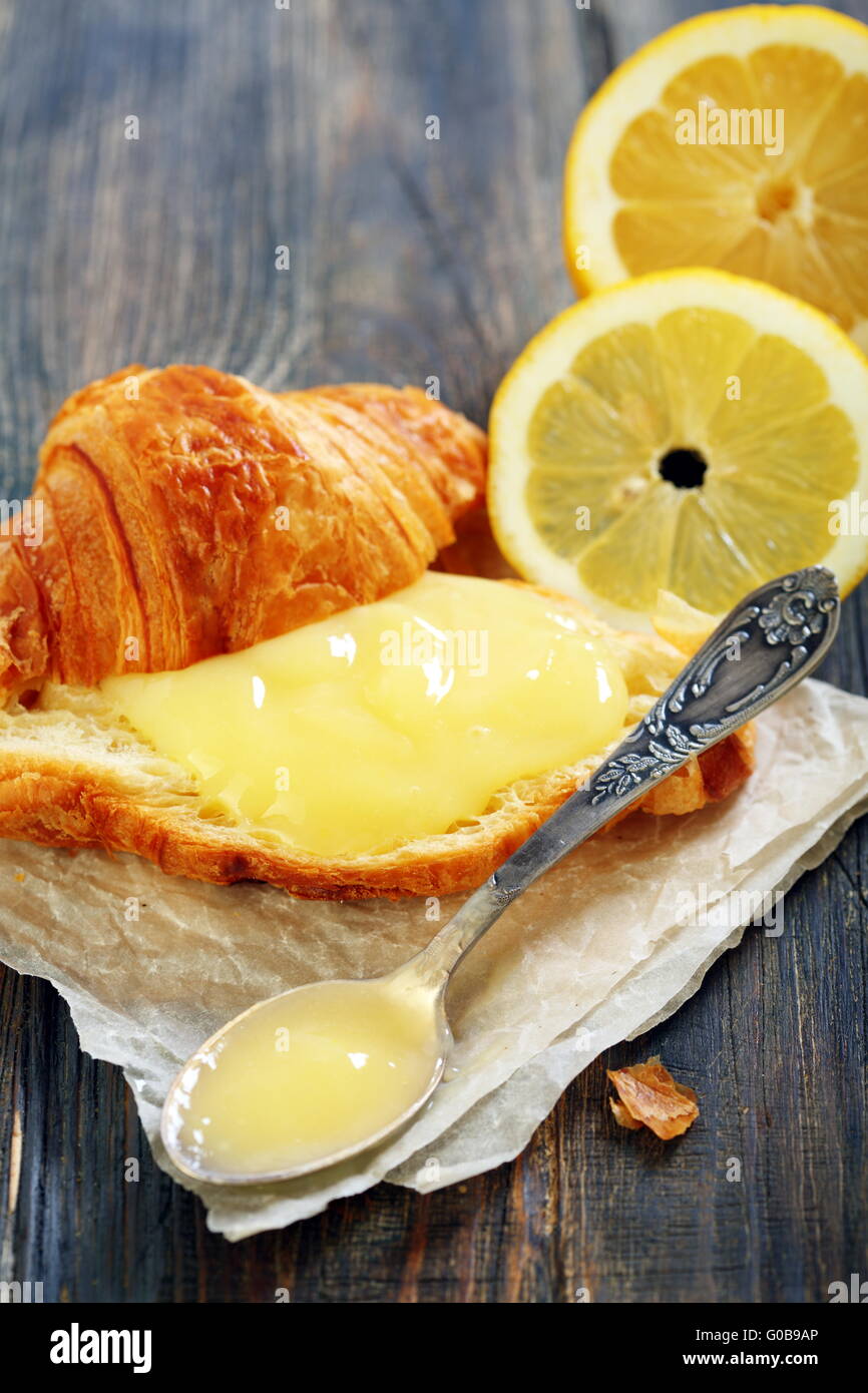 Lemon curd and teaspoon on a slice of fresh croissant. Stock Photo